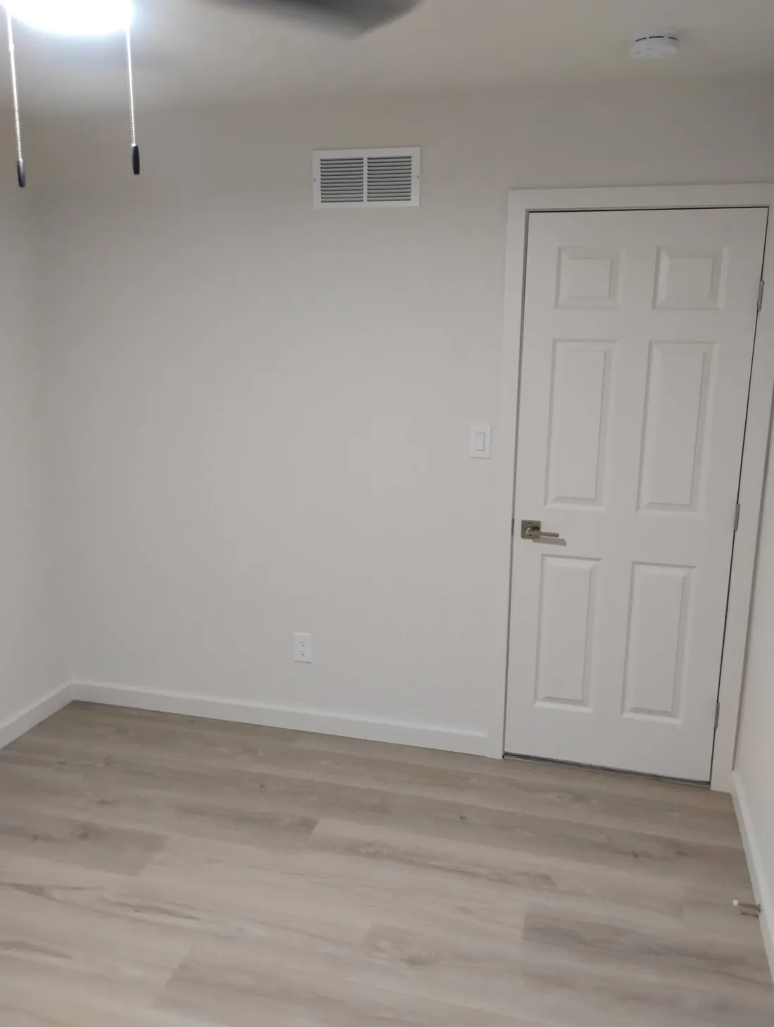Same bedroom after, with fresh neutral walls, white trim and a repainted door